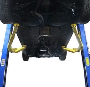 Car lifted on hydraulic lift showing undercarriage and suspension system.