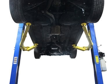 Car lifted on hydraulic lift showing undercarriage and suspension system.